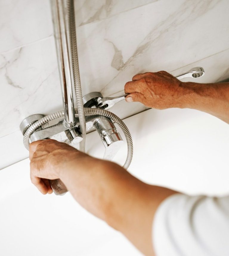 Yanar Haustechnik - Notdienst Eine Person repariert einen Wasserhahn an einer weißen Fliesenwand.