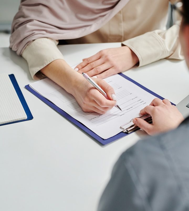 Yanar Haustechnik - Förderung Eine Person schreibt mit einem Stift auf ein Formular zur Förderungsberatung, eine andere Person schaut zu.